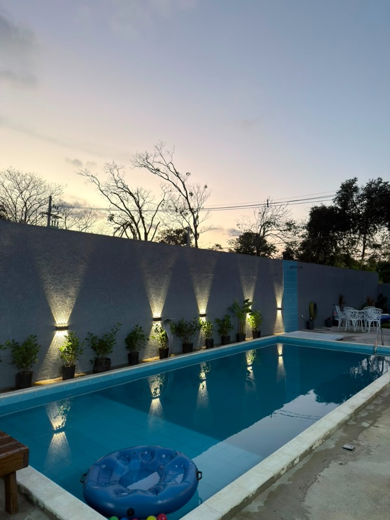 Piscina ao entardecer com jardim iluminado no Espaço Canto dos Pássaros